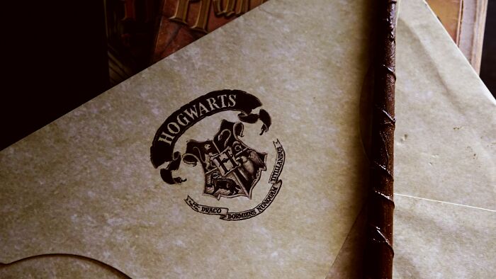 Obálka s pečaťou Rokfortu vedľa kúzelníckej paličky, symbolizuje magický svet Harryho Pottera.