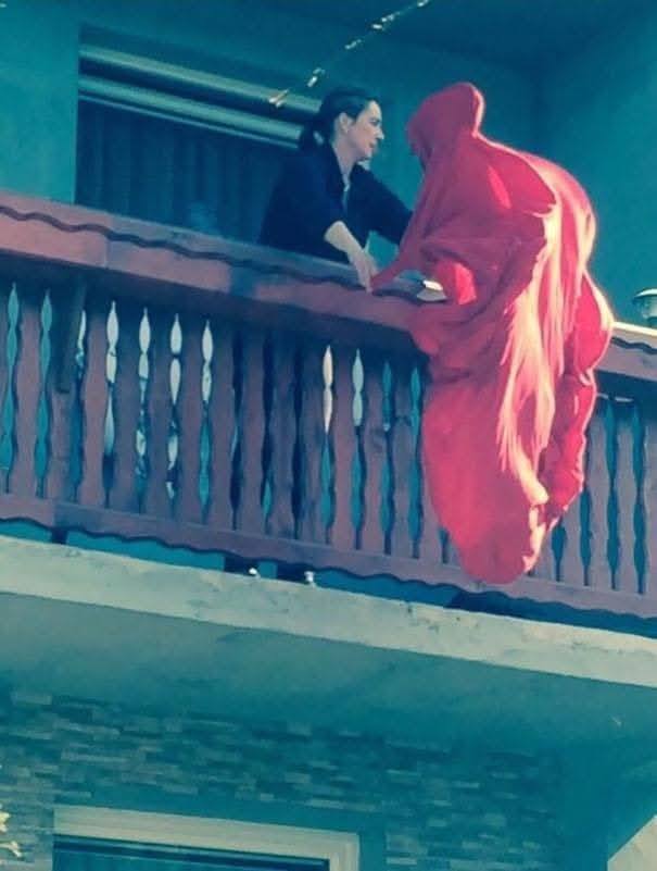 Osoba na balkóne podáva ruku osobe v červenom plášti.