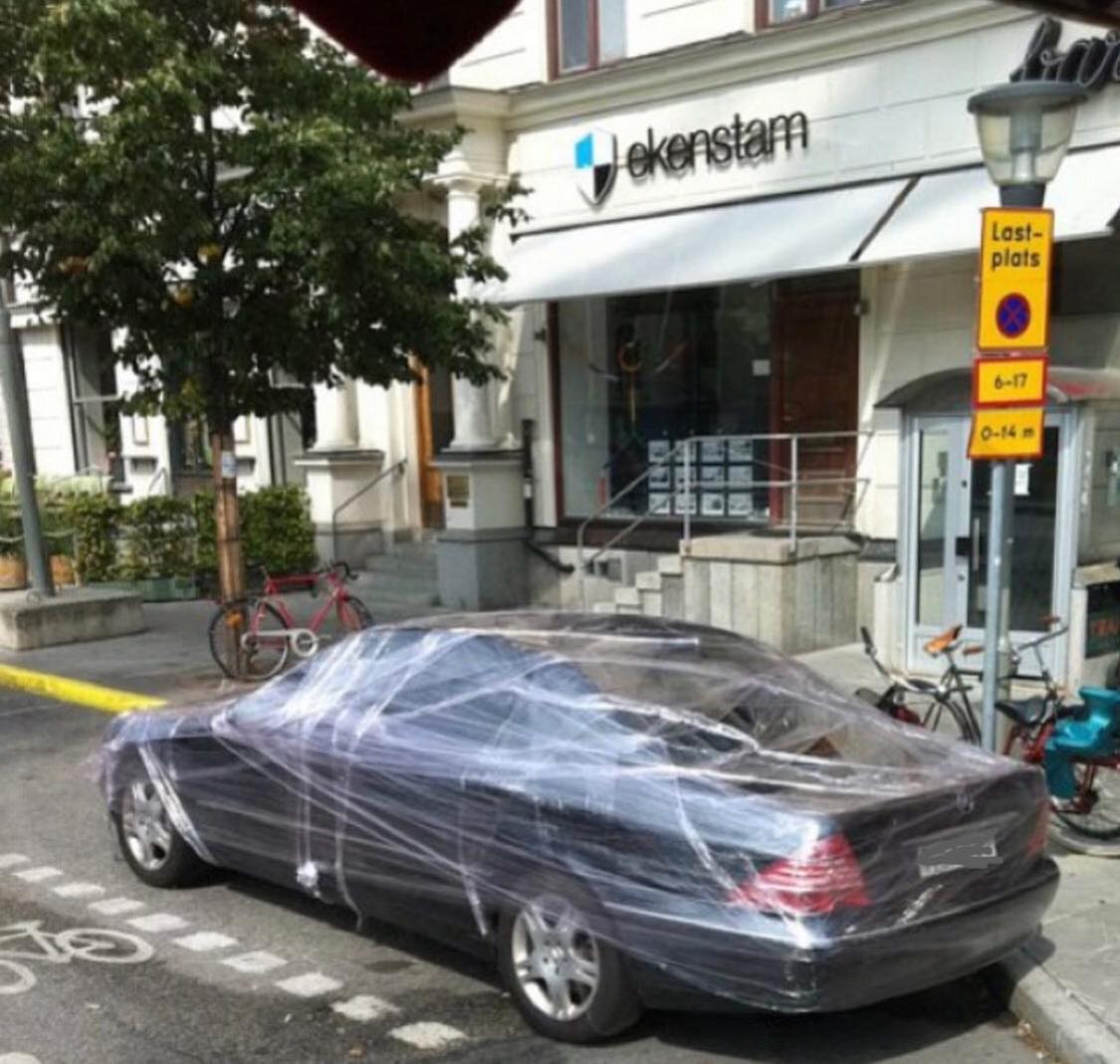 Auto zaparkované na cyklotrase, obalené fóliou, pred budovou s nápisom „ekenstam“.