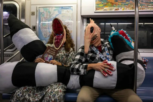 Dve osoby v kreatívnych kostýmoch Beetlejuice v metre s kostýmovým rekvizitami v tvare pruhovaného hada.