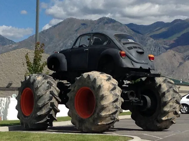 Čierne auto na obrovských terénnych kolesách zaparkované pred horskou scenériou.