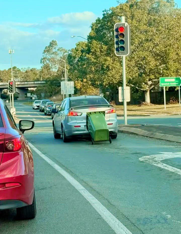 Auto so zaseknutým kontajnerom vzadu stojí na križovatke pod červeným svetlom.