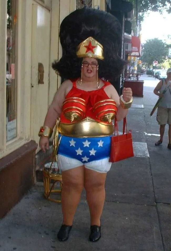 Osoba v originálnom kostýme Wonder Woman stojí na ulici s veľkou parochňou a zlatými doplnkami.