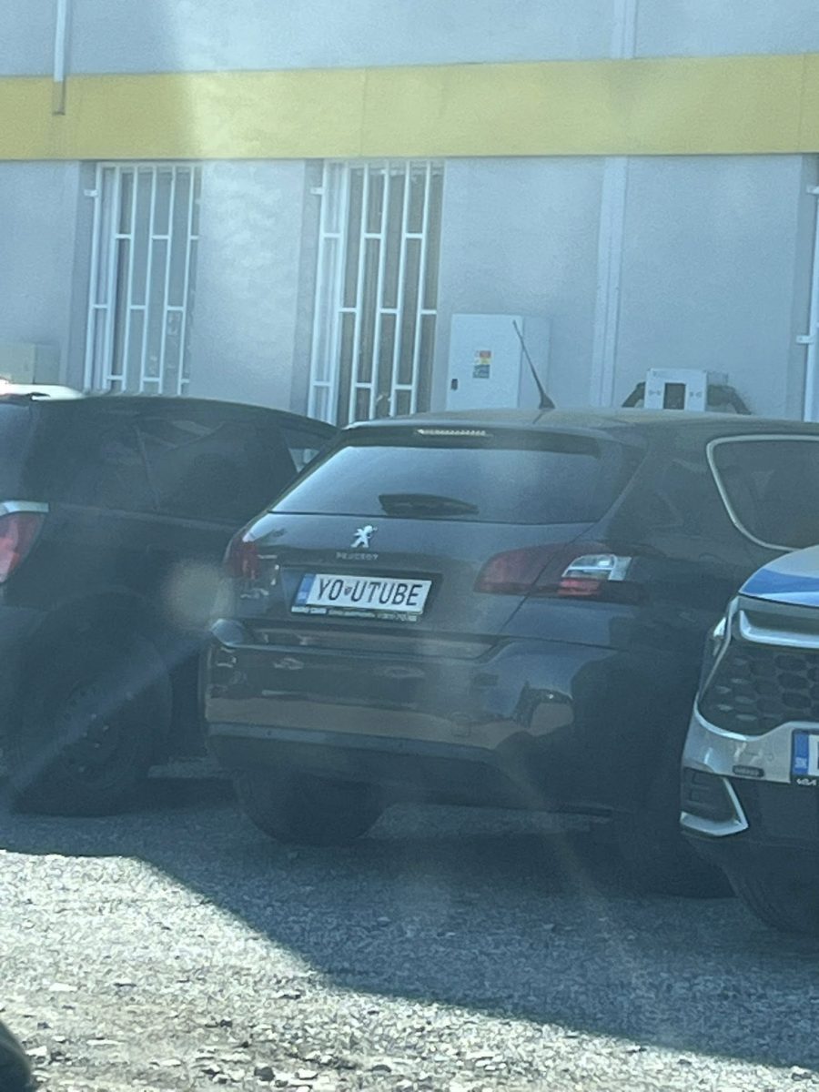 Auto so ŠPZ YOUTUBER zaparkované medzi dvoma vozidlami pred budovou so žltým pásom.