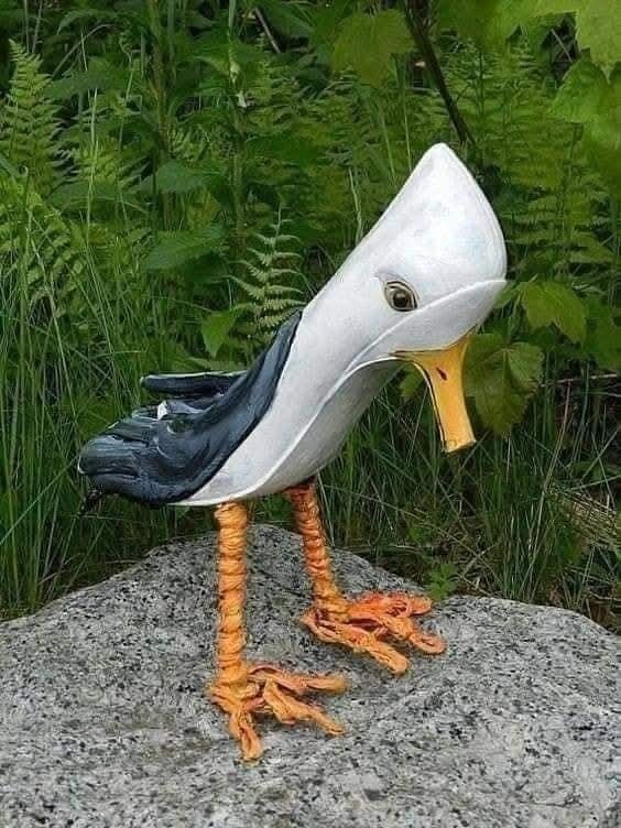 Originálna plastika vtáka s dlhými oranžovými nohami stojí na kameni v prírodnom prostredí.