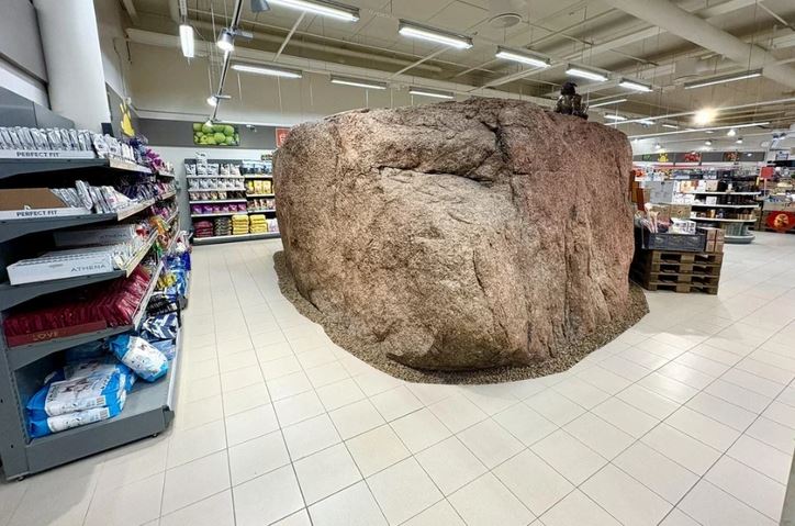 Obrovský kameň v strede supermarketu medzi regálmi s tovarom a upraveným osvetlením.