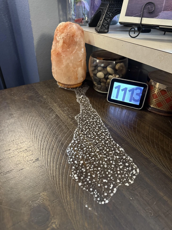 Soľná lampa na drevenom stole a vedľa nej stopa bieleho prášku. Vedľa leží digitálny displej s časom 11:13.