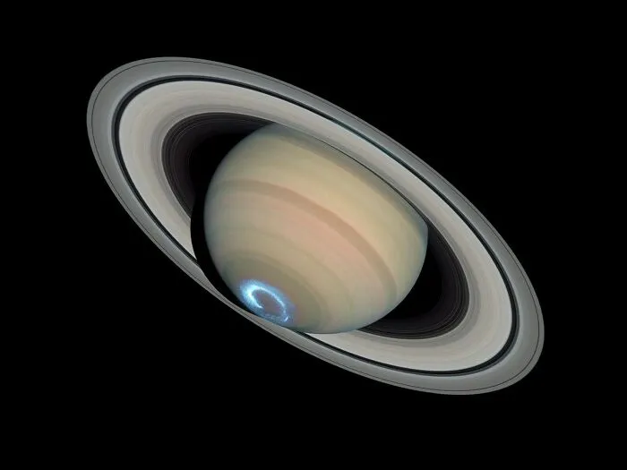Planéta Saturn s charakteristickými prstencami a polárnou žiarou na severnom póle v tmavom vesmíre.