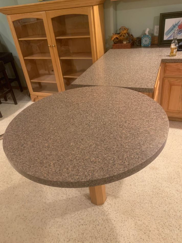 Kuchynský kút s okrúhlym stolom a skrinkou z dreva s policami na pozadí.