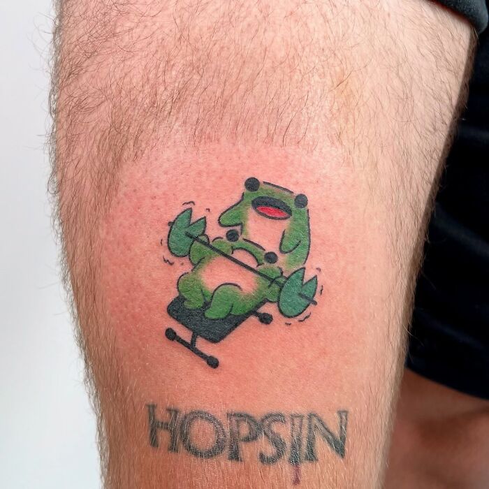 Zelená kreslená postavička na tetovaní na nohe, pod ňou nápis Hopsin.