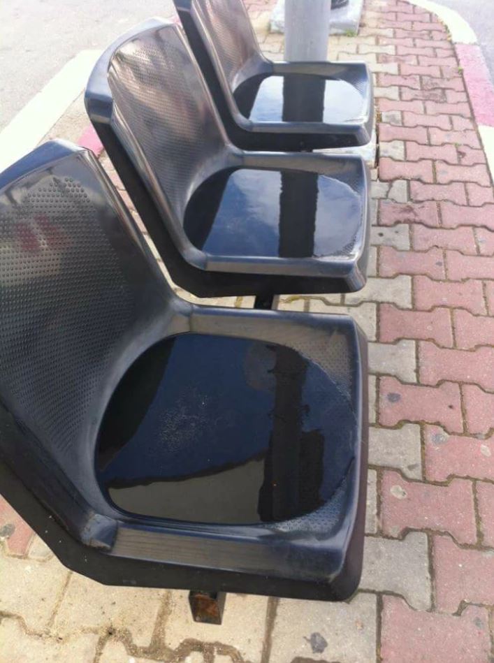 Tri mokré plastové stoličky na autobusovej zastávke po daždi, zrkadliace okolie na povrchu.