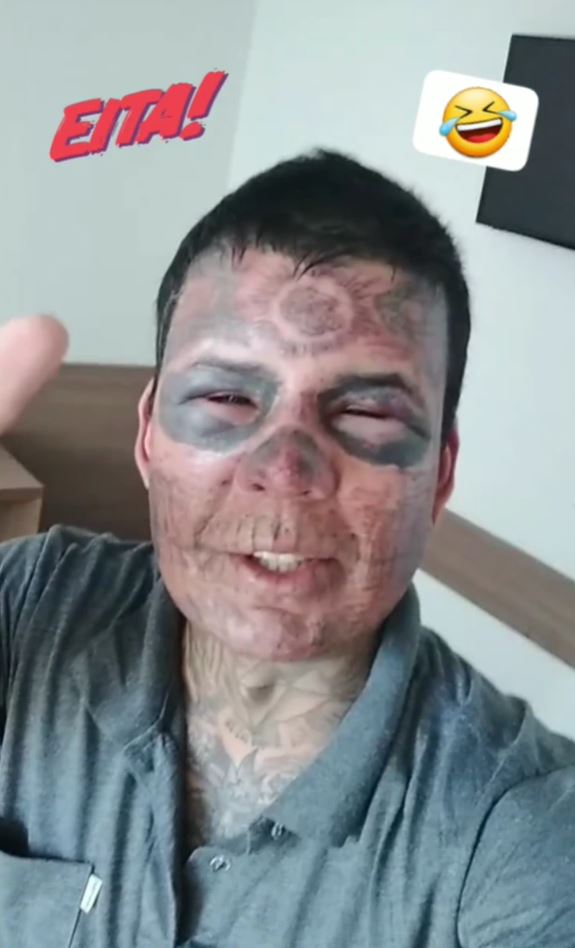 Osoba so silnými tvárovými tetovaniami sa usmieva a ukazuje gesto palcom hore.