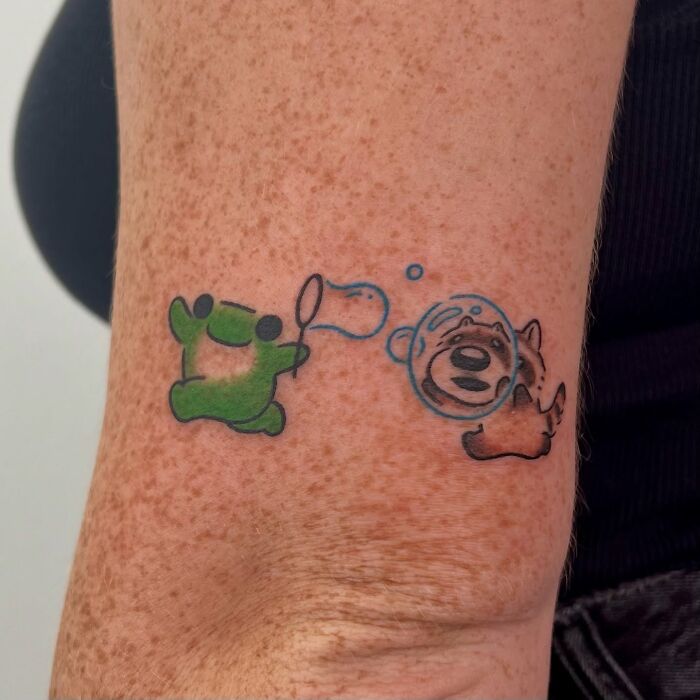 Žaba a medveď vyškerene v bublifuku na tetovaní na ruke. Farebné hravé scény na koži človeka.
