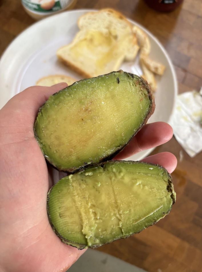 Polovička zrelého avokáda v ruke, pripravená na toast na bielom tanieri.