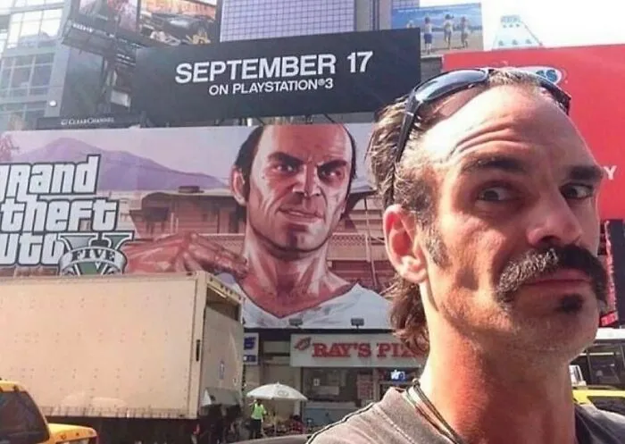 Muž pred billboardom s reklamou na hru Grand Theft Auto V, vydanie na PlayStation 3, dátum uvedenia 17. september.