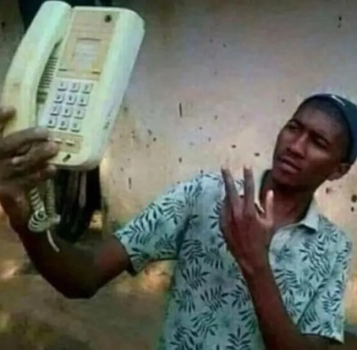 Muž drží starý telefón ako selfie, vyzerá zmätene. Nechapavý výraz na tvári, telefón s káblom v ruke.