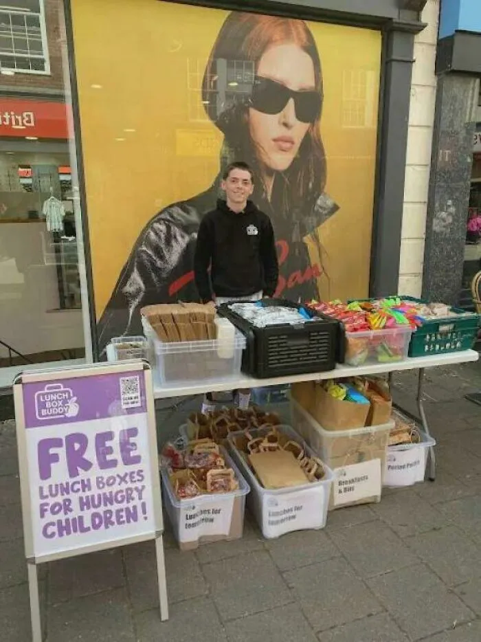 Muž ponúka bezplatné obedy pre deti. Stojí pri stole s krabicami plnými jedla pred obchodom.