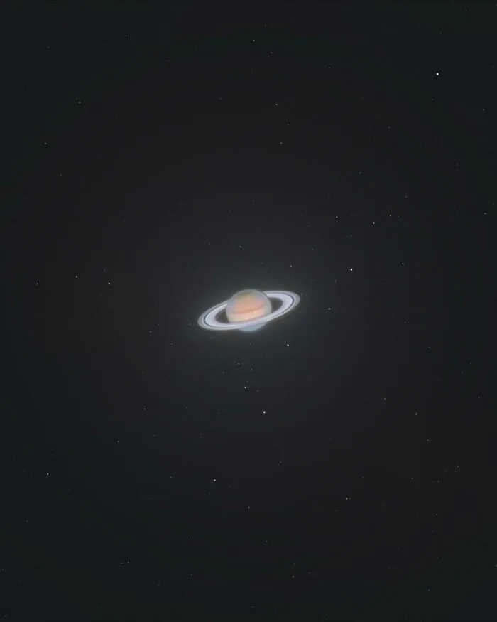 Planéta Saturn s viditeľnými prstencami na nočnej oblohe, obklopená drobnými hviezdami.