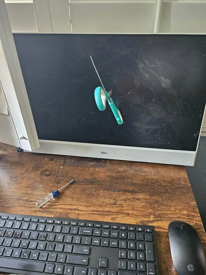 Počítačový monitor s nožnicami v obrazovke, klávesnica a myš na drevenom stole.