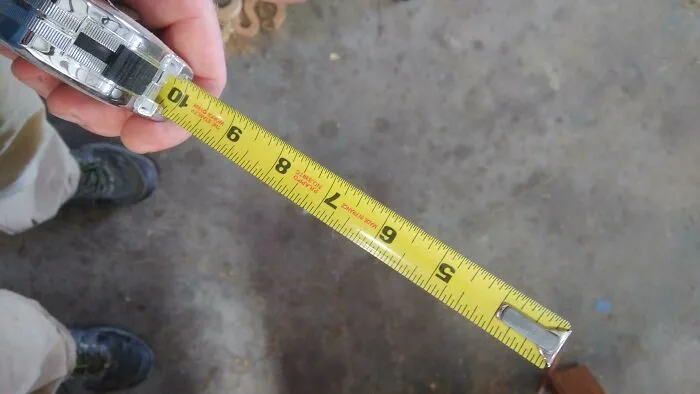 Osoba drží zvinovací meter, meria vzdialenosť na podlahe.