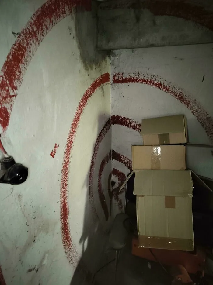 Tmavá miestnosť s krabicami a červenou špirálou na stene. Tajomná a záhadná atmosféra.