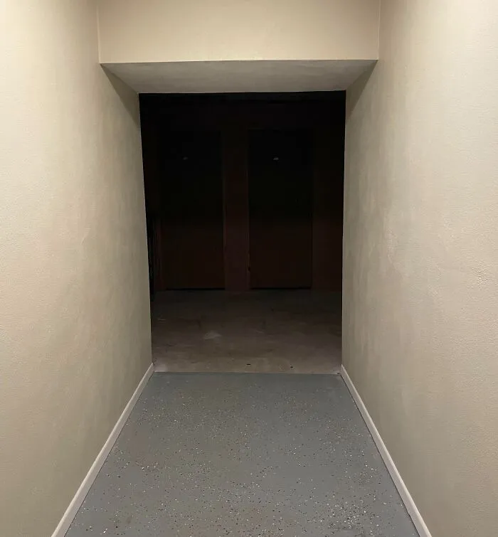 Tmavý chodba so svetlými stenami vedúca do neosvetlenej miestnosti, minimalistický dizajn.