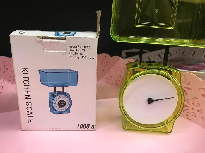 Zelená kuchynská váha s bielym číselníkom a obalom, kapacita 1000 g.