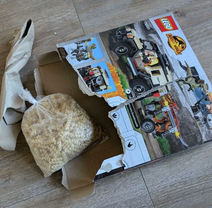 Roztrhaná krabica LEGO s vreckom náhradných dielov položená na podlahe.