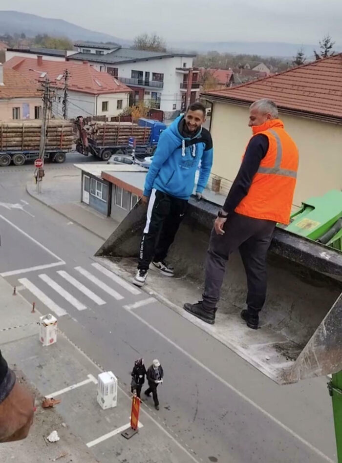 Muži stojaci v lyžici bagra nad ulicou s pohľadom na malebnú dedinu.