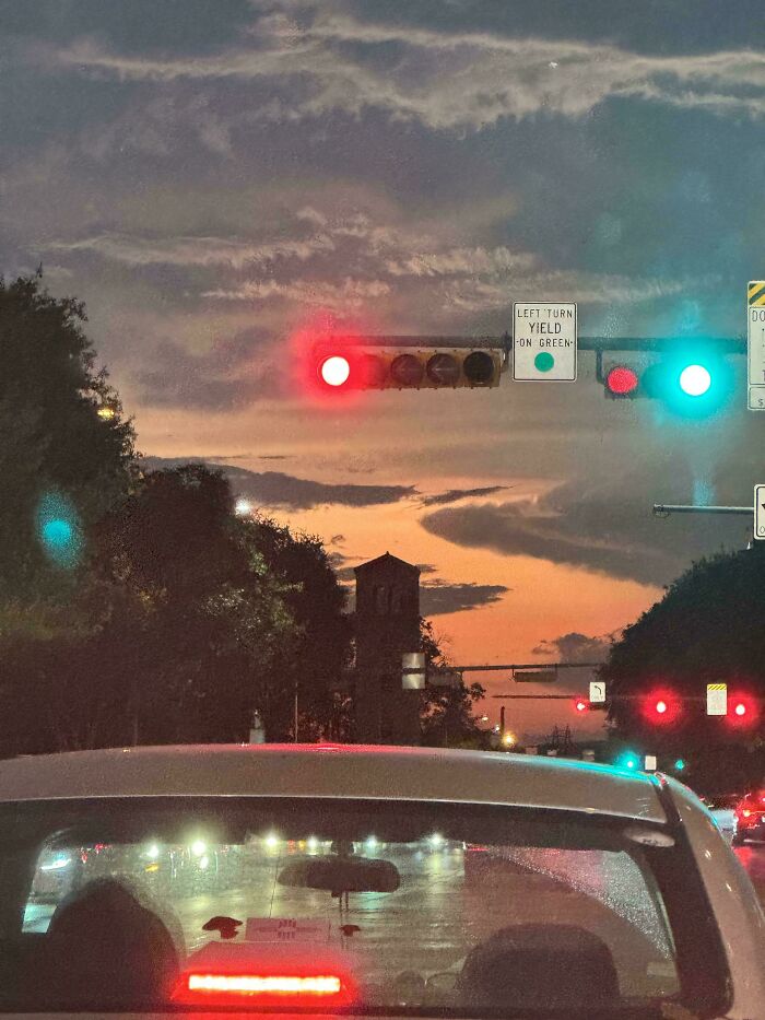 Auto na semafore pri západe slnka, obloha s oblakmi a farebné svetlá zvýrazňujú atmosféru večerného mesta.