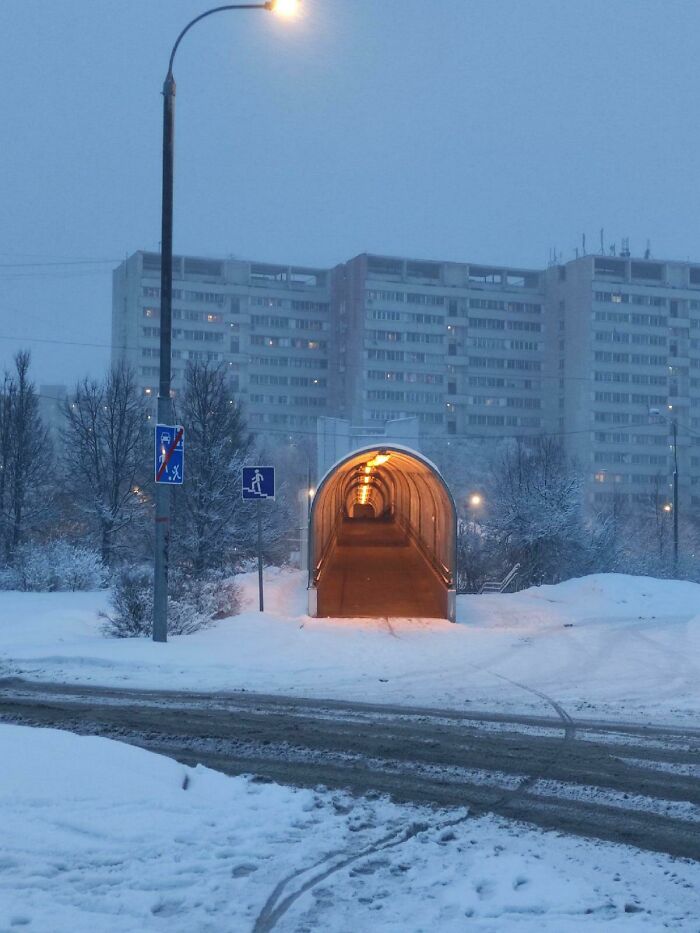 Osvetlený tunel pre chodcov pokrytý snehom s panelákom v pozadí. Zimná scenéria v mestskom prostredí.