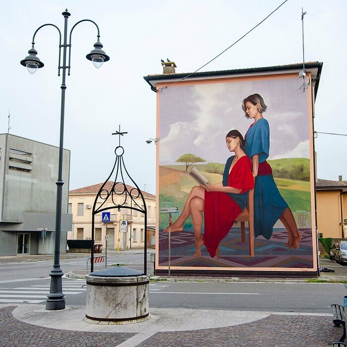 Mural dvoch žien s knihou na stene budovy v tichom mestskom prostredí.