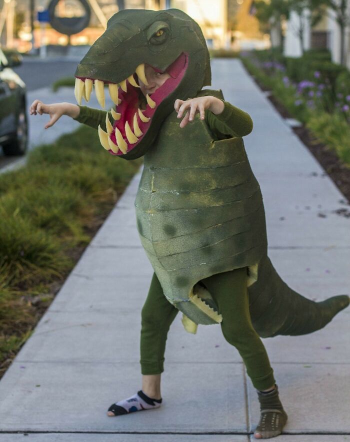 Dieťa v kostýme dinosaura na chodníku.