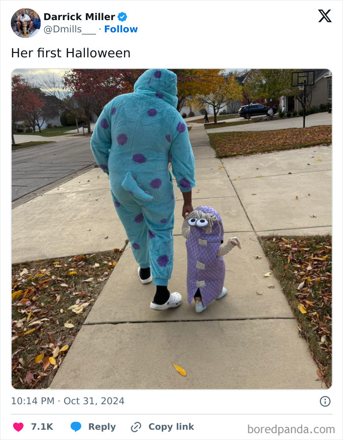 Otec a dieťa v kostýmoch na Halloween kráčajú po chodníku medzi pestrofarebnými jesennými stromami.