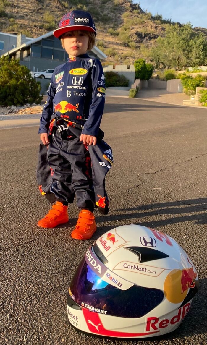 Dieťa v pretekárskej kombinéze Red Bull so závodnou helmou na ceste pred domom.