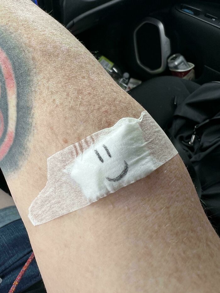 Náplasť s úsmevom na ruke, viditeľná tetováž a pozadie interiéru auta.