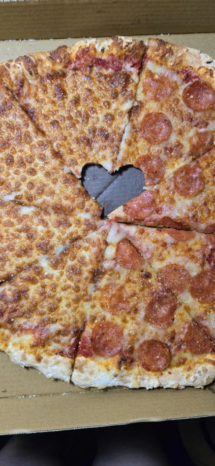 Pizza so syrom a salámou, srdcový výrez uprostred, v kartónovej krabici.