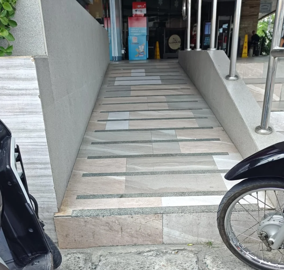 Rampový vstup s kamenitou podlahou vedľa motorky vedie do obchodu.