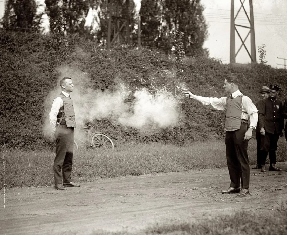 Muž v nepriestrelnej veste počas testu strelby, začiatok 20. storočia, historický experiment na otvorenom priestranstve.
