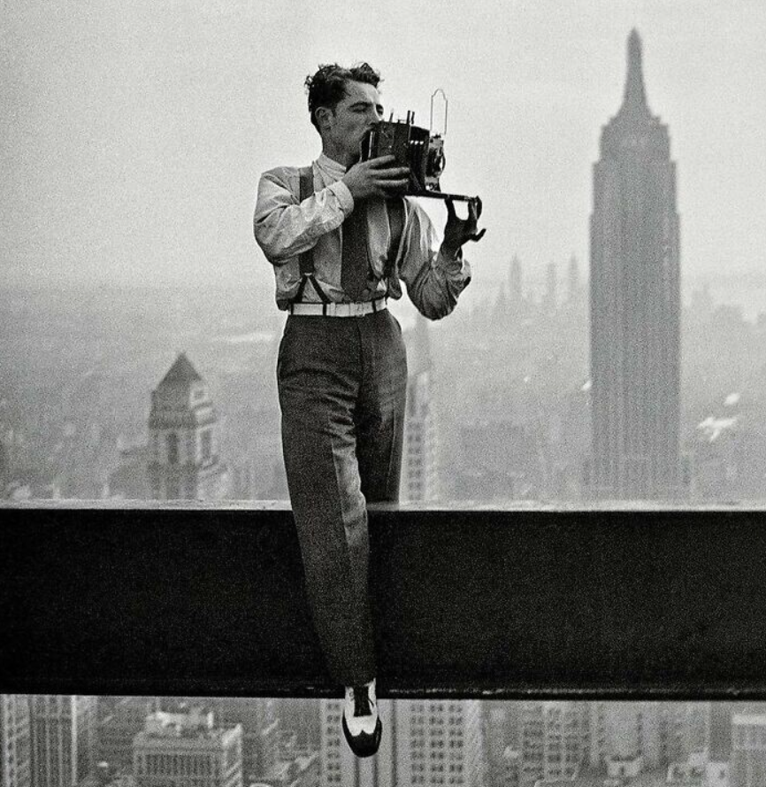 Muž fotí z konštrukčnej oceľovej nosníka v New Yorku, v pozadí Empire State Building.