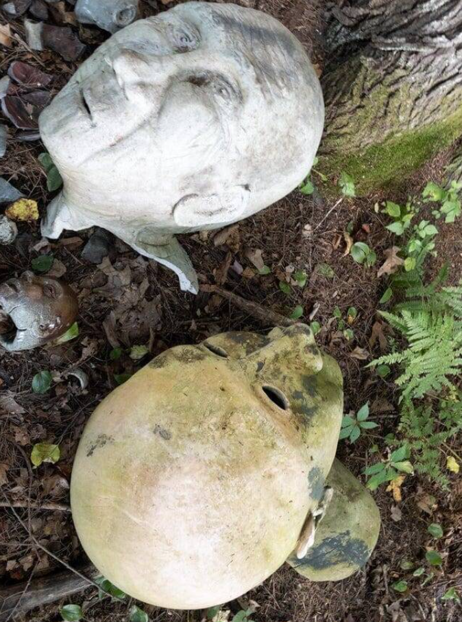 Dve veľké sochárske hlavy ležia na zemi v lese medzi lístím a machom.