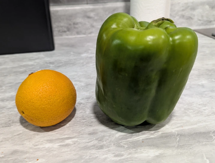 Veľká zelená paprika vedľa pomaranča.