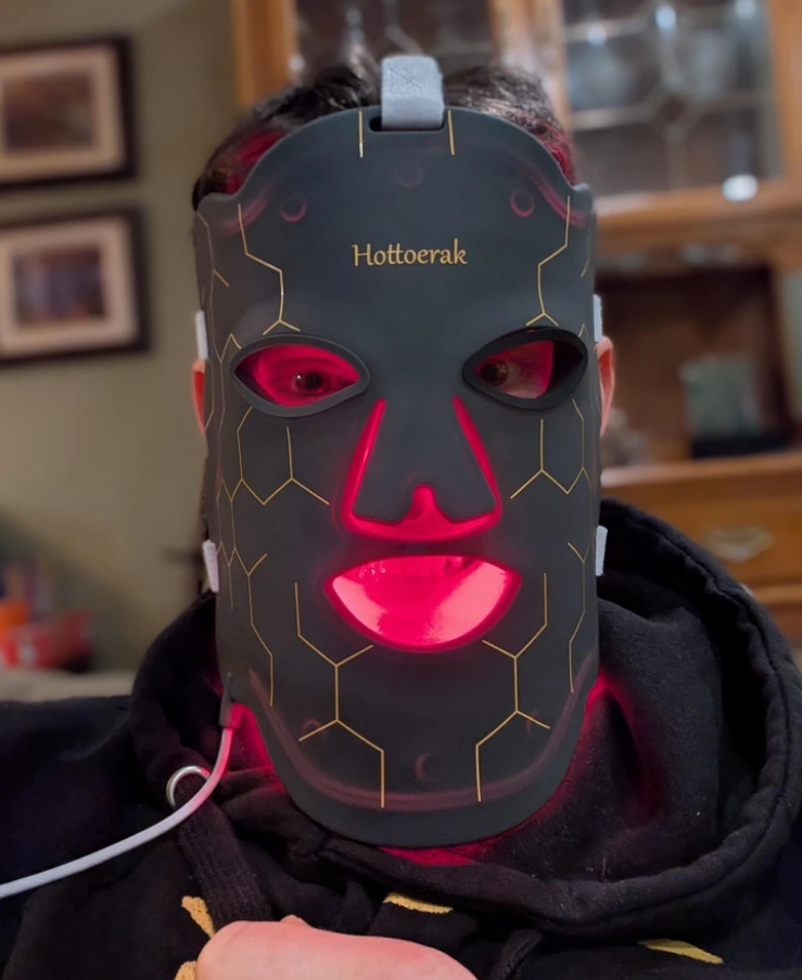 Osoba s nositeľnou LED maskou na tvár pre terapiu svetlom, obklopená tlmeným osvetlením interiéru.
