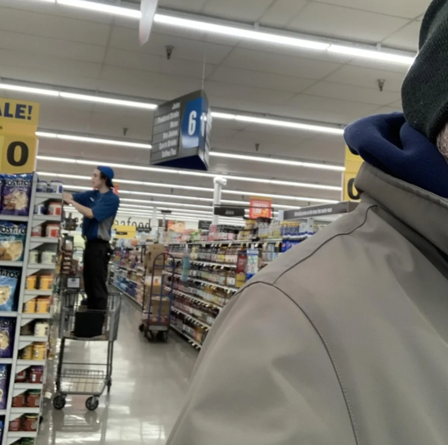 Pracovník v obchode stojí na vozíku a dopĺňa tovar na regály v supermarkete.