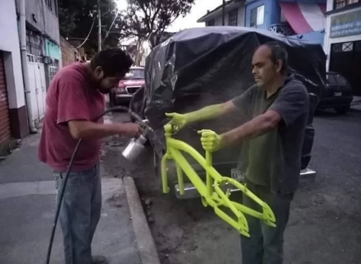 Muž strieka na ulici žltou farbou rám bicykla, druhý muž ho drží.