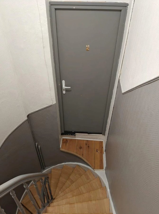 Úzke točité schody vedúce k sivo-bielym dverám v malom priestore.