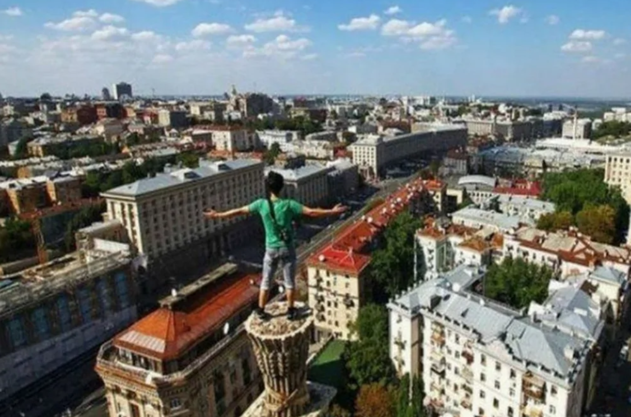 Osoba stojí na budove, rozprestiera ruky a obdivuje panorámu mesta pod jasnou oblohou s oblakmi.