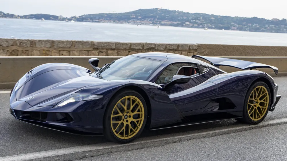 Luxusný superšportový automobil s elegantným dizajnom a zlatými kolesami jazdí po prímorskej ceste.