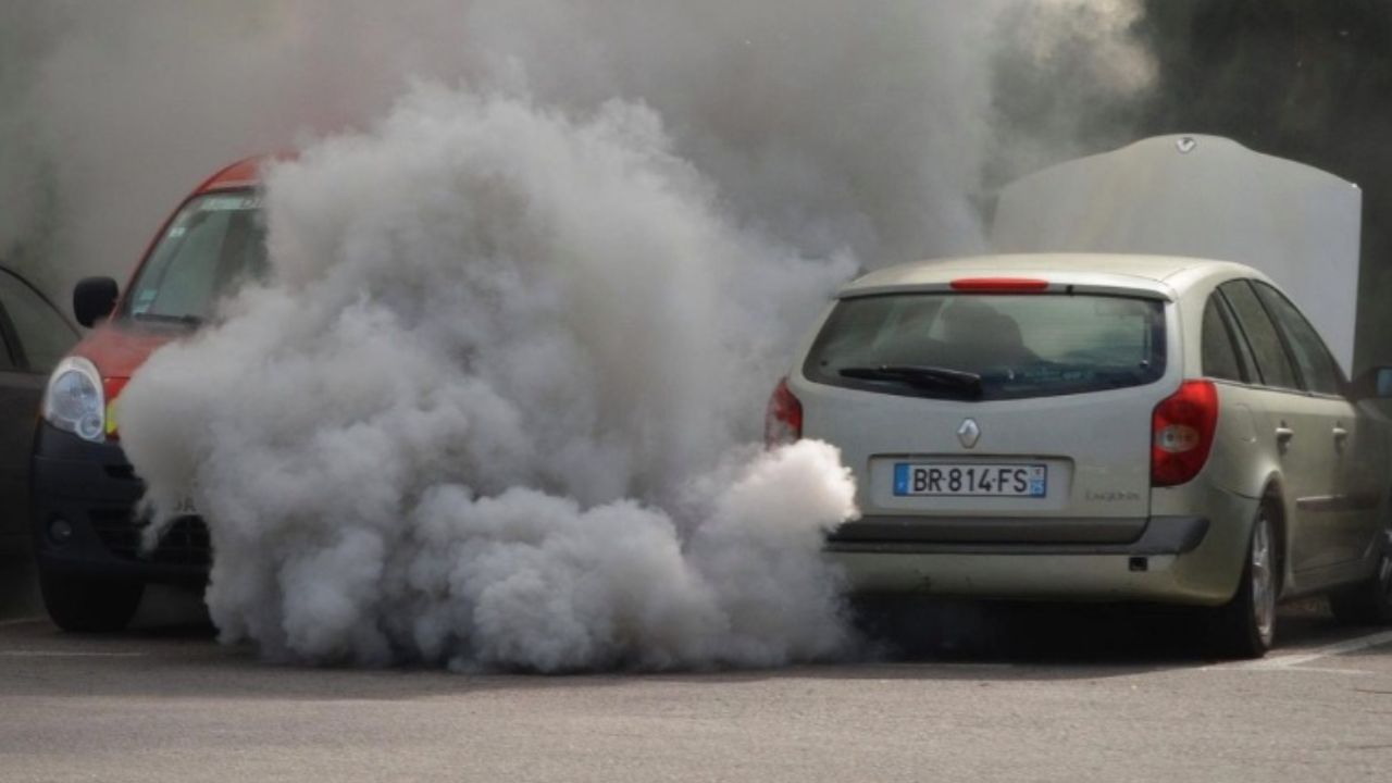 Dym z auta na parkovisku, autá obalené hustým bielym oblakom. Autonehoda či porucha na verejnom mieste.