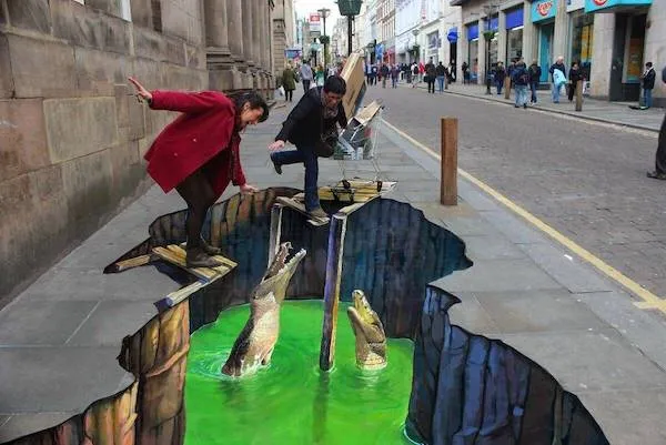 Pouličné 3D umenie s krokodílmi v žiarivo zelenej rieke zdanlivo prepadnutej v chodníku, ľudia pózujú na okraji.